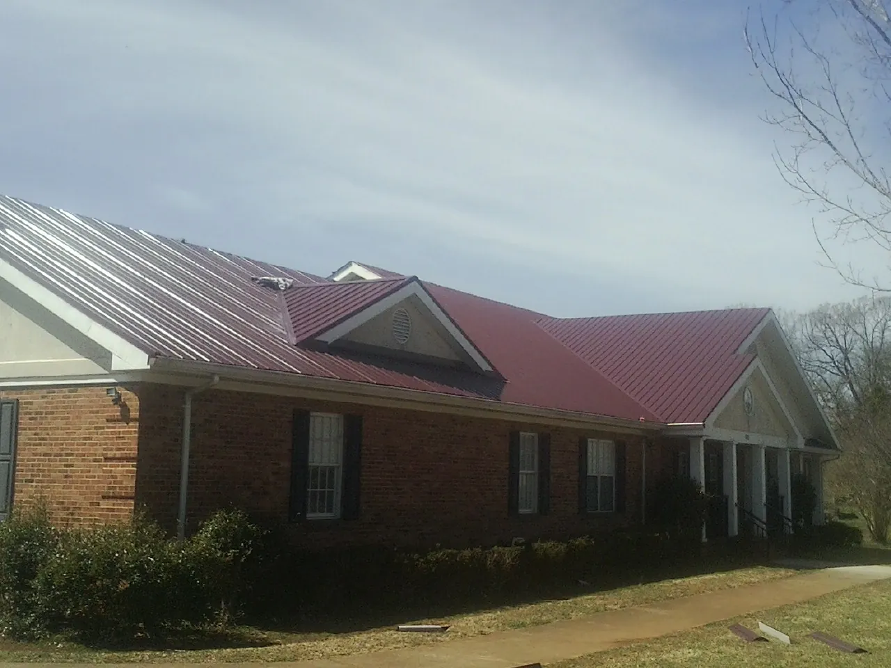 Red metal roof with gabled entries on a long brick building, from a Hail Damage Roof Repair job in Detroit