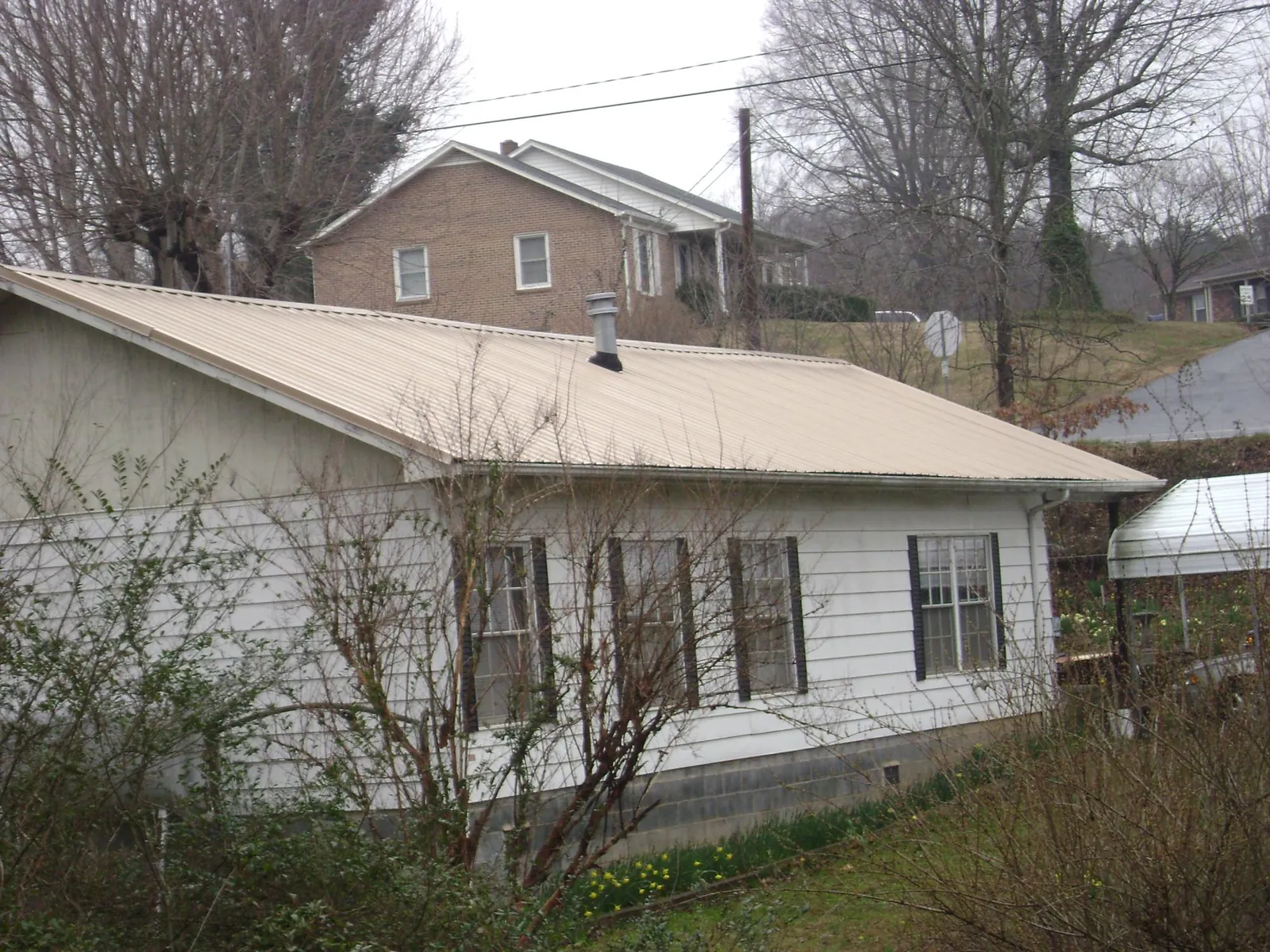 Tan metal roof on a white sided house set into a hillside — Commercial Roofing by Roofing Brothers in Detroit